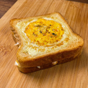 Egg-in-a-hole toast with melted cheese served on a wooden board.