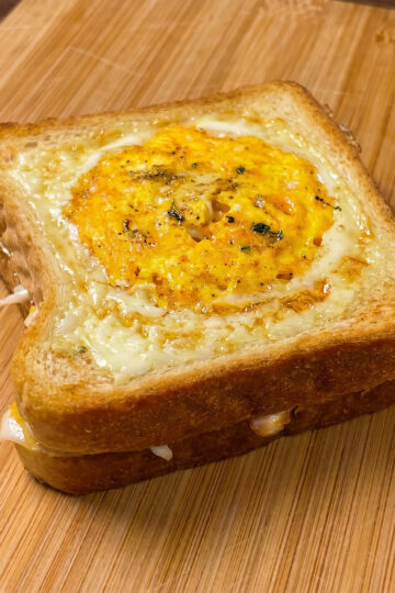 Egg-in-a-hole toast with melted cheese served on a wooden board.
