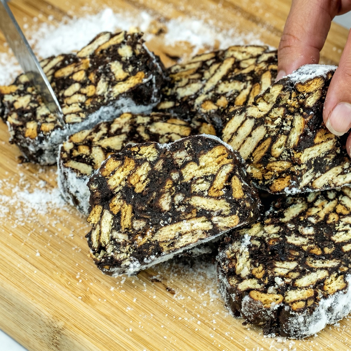 Hand holding a slice of chocolate salami with crunchy cookie pieces.