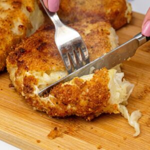 Crispy fried cabbage steak being cut open with a knife and fork.