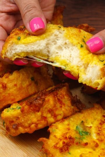 Hand holding a crispy fried bread slice with a soft cheesy center.