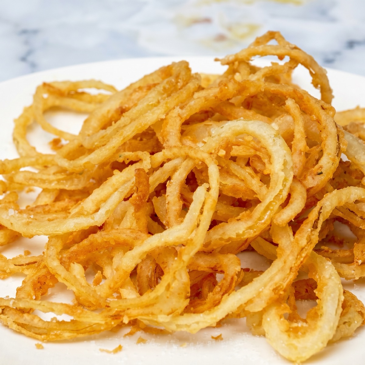 Close-up of crispy fried onions served on a white plate, golden brown and crunchy.