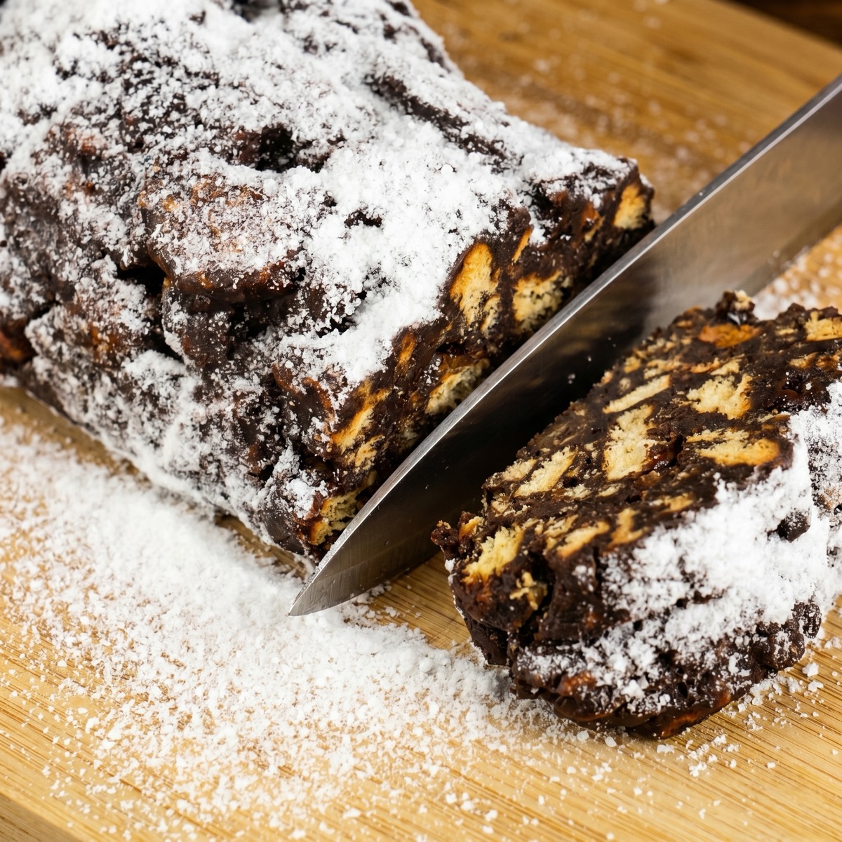 Knife slicing a no-bake chocolate salami coated with powdered sugar.