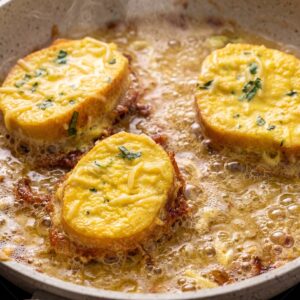 Bread slices frying in hot oil with a cheesy egg coating and parsley.