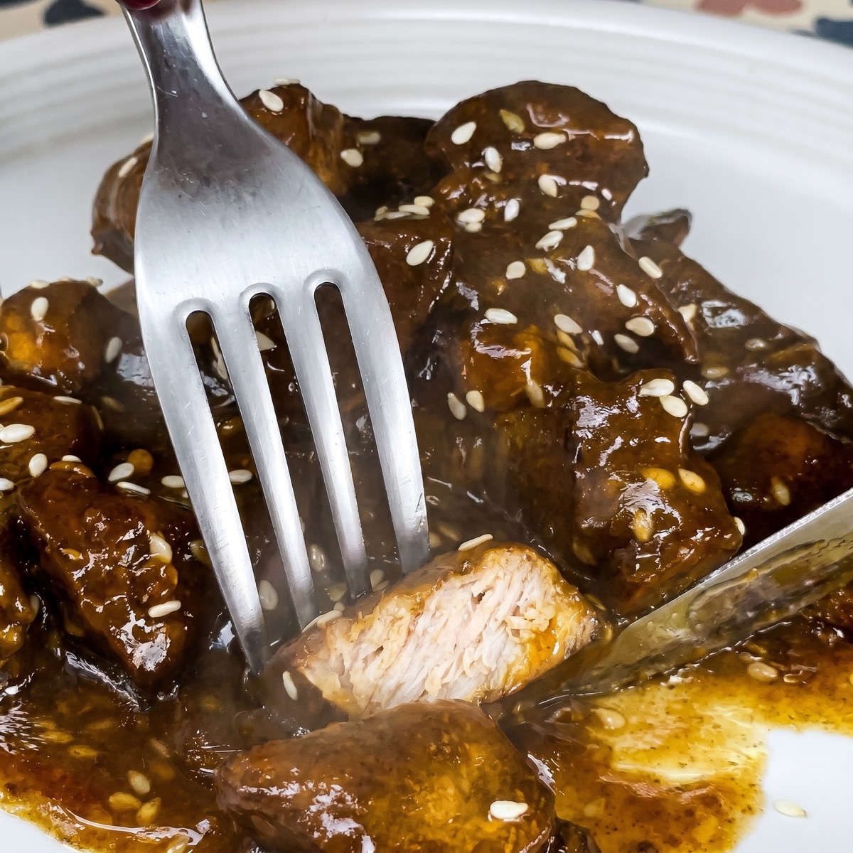 Fork lifting a juicy pork tenderloin bite covered in a silky soy honey sauce.
