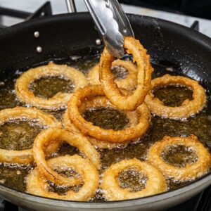 Golden onion rings being lifted from hot oil with tongs during frying.