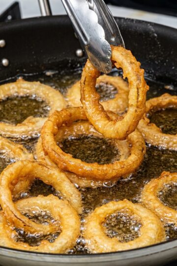 Golden onion rings being lifted from hot oil with tongs during frying.