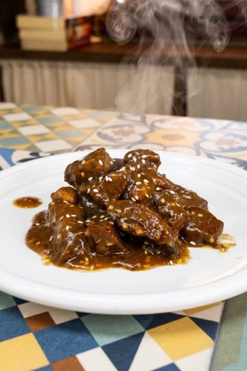 Fork cutting into pork tenderloin bites coated in a glossy sauce and topped with sesame seeds.