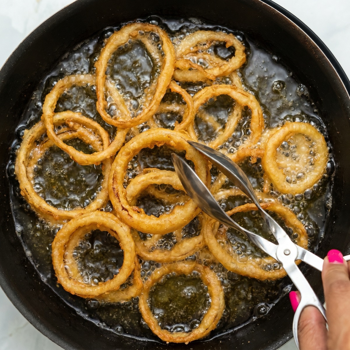Homemade onion rings frying in hot oil in a skillet until golden and crispy.