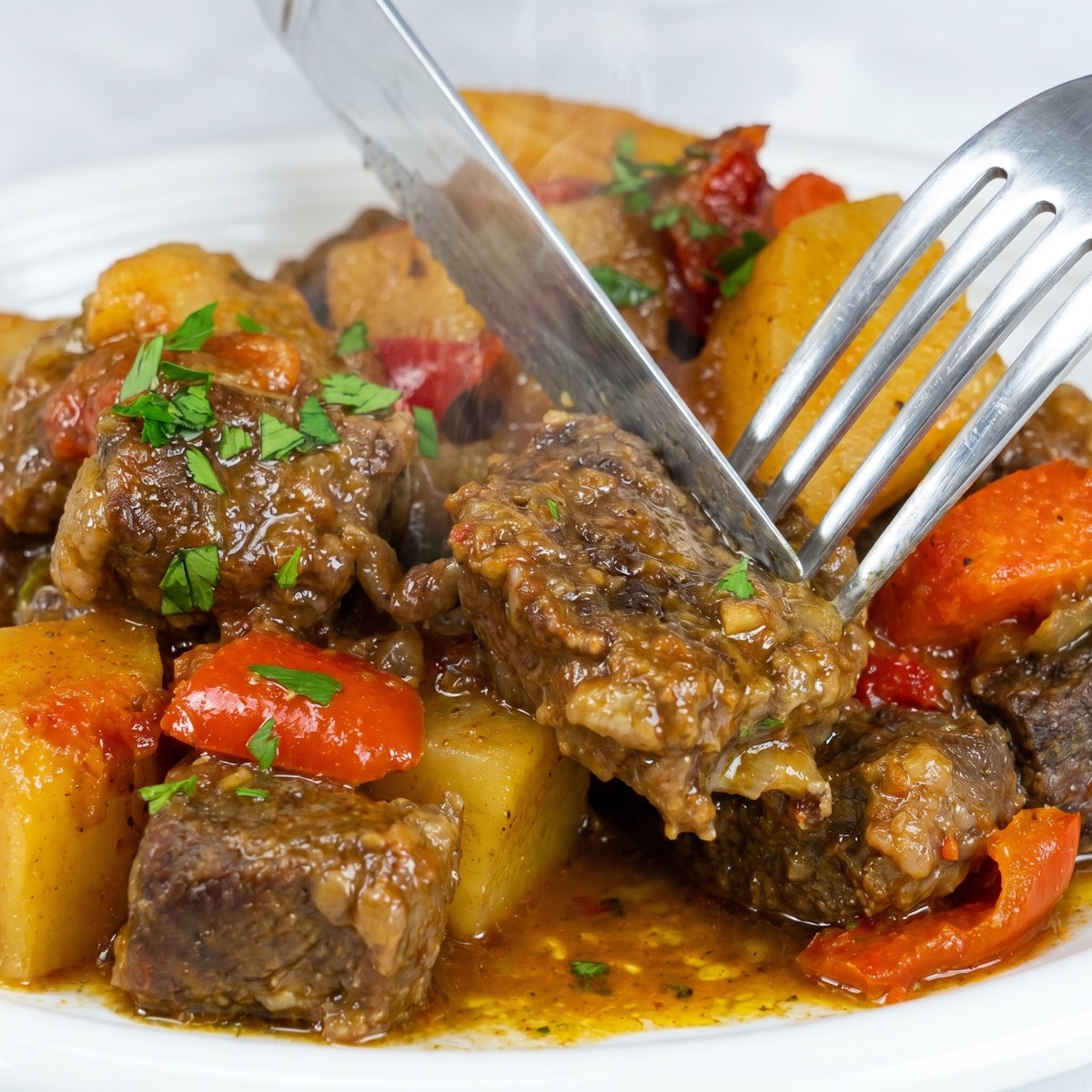 Oven-baked beef and vegetables served with sauce and fresh parsley.