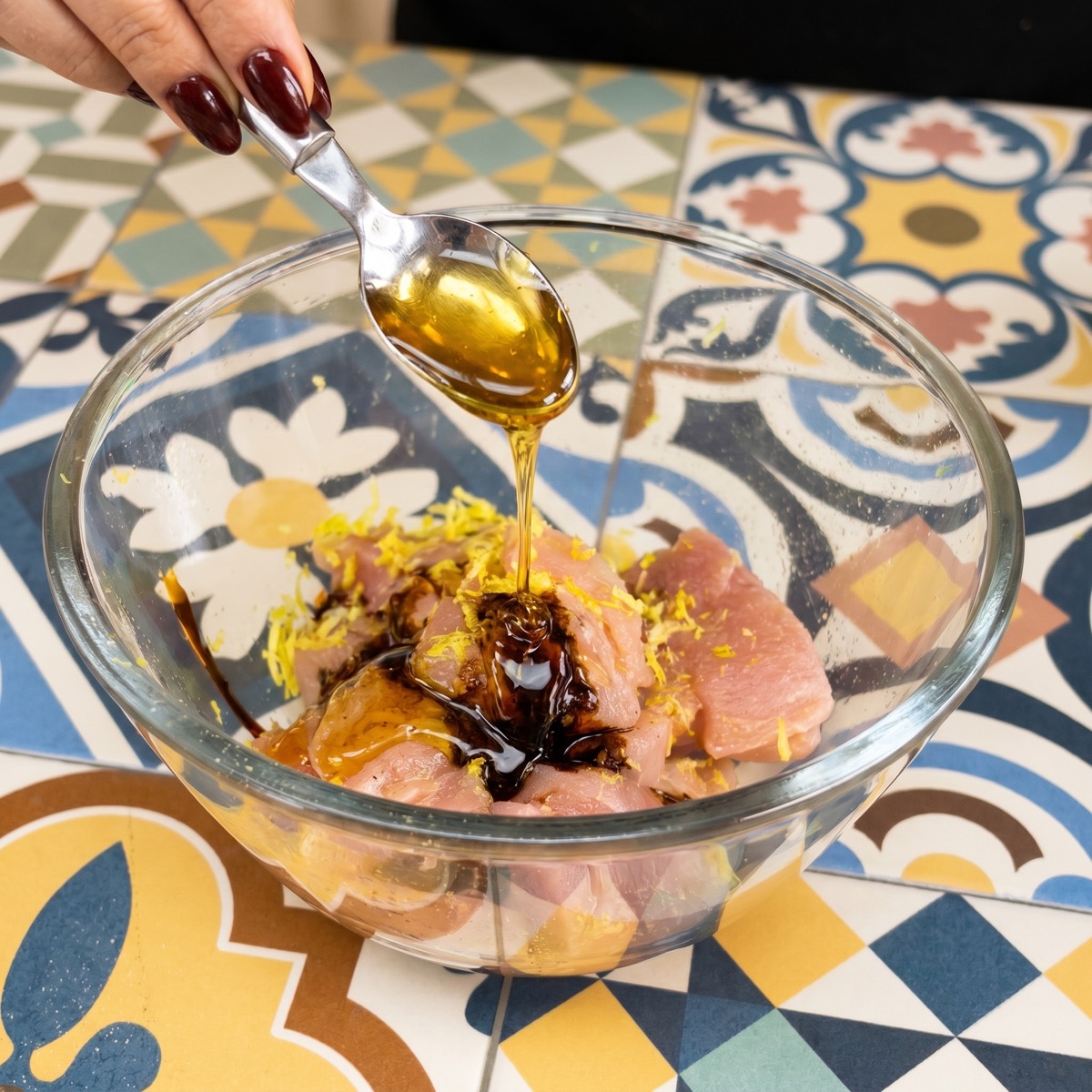 Honey and soy sauce being added to pork tenderloin pieces with lemon zest in a glass bowl.