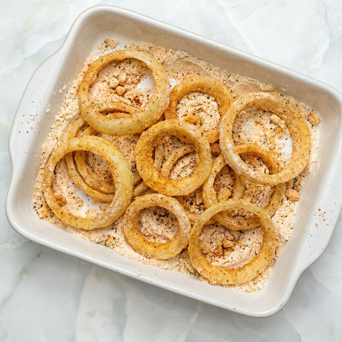 Raw onion rings coated in seasoned flour before frying for a crispy texture.