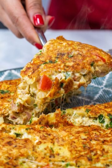 Slice of cheesy tuna omelette being lifted from a plate with melted mozzarella.