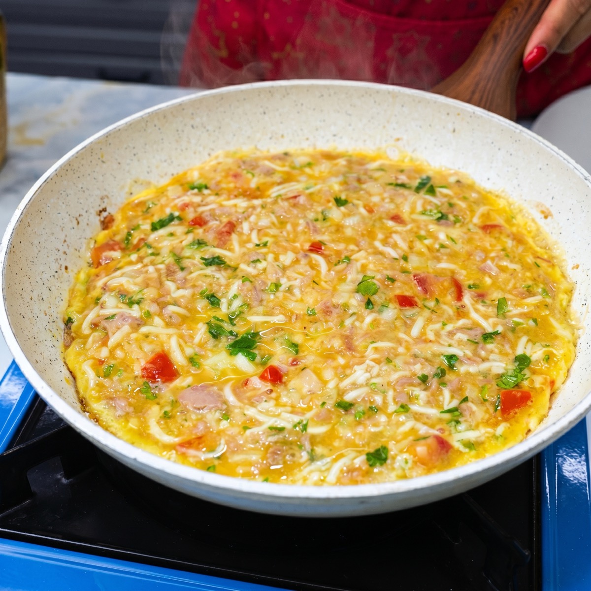 Tuna omelette mixture with eggs, tomato, onion, mozzarella, and herbs cooking in a skillet.