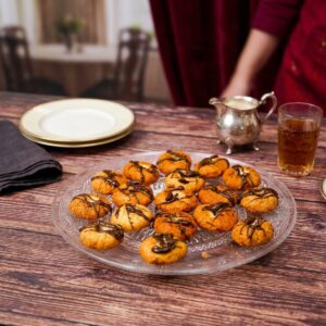Chocolate bread donuts ready in a glass dish with a silver teapot and a glass of tea on a wooden table.