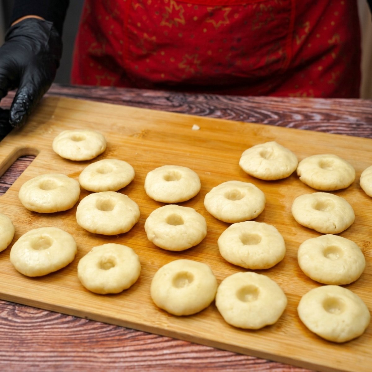 Chocolate bread donut dough shaped into rings on a light wooden board.