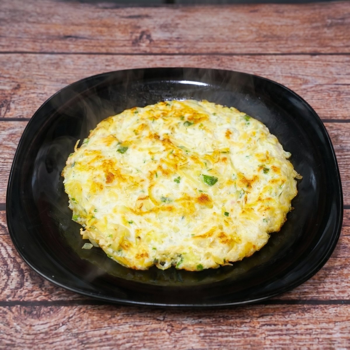 Hähnchen-Kartoffel-Omelett mit Eiern und geriebenen Kartoffeln, mit frischen Kräutern bestreut und auf einem Teller serviert.