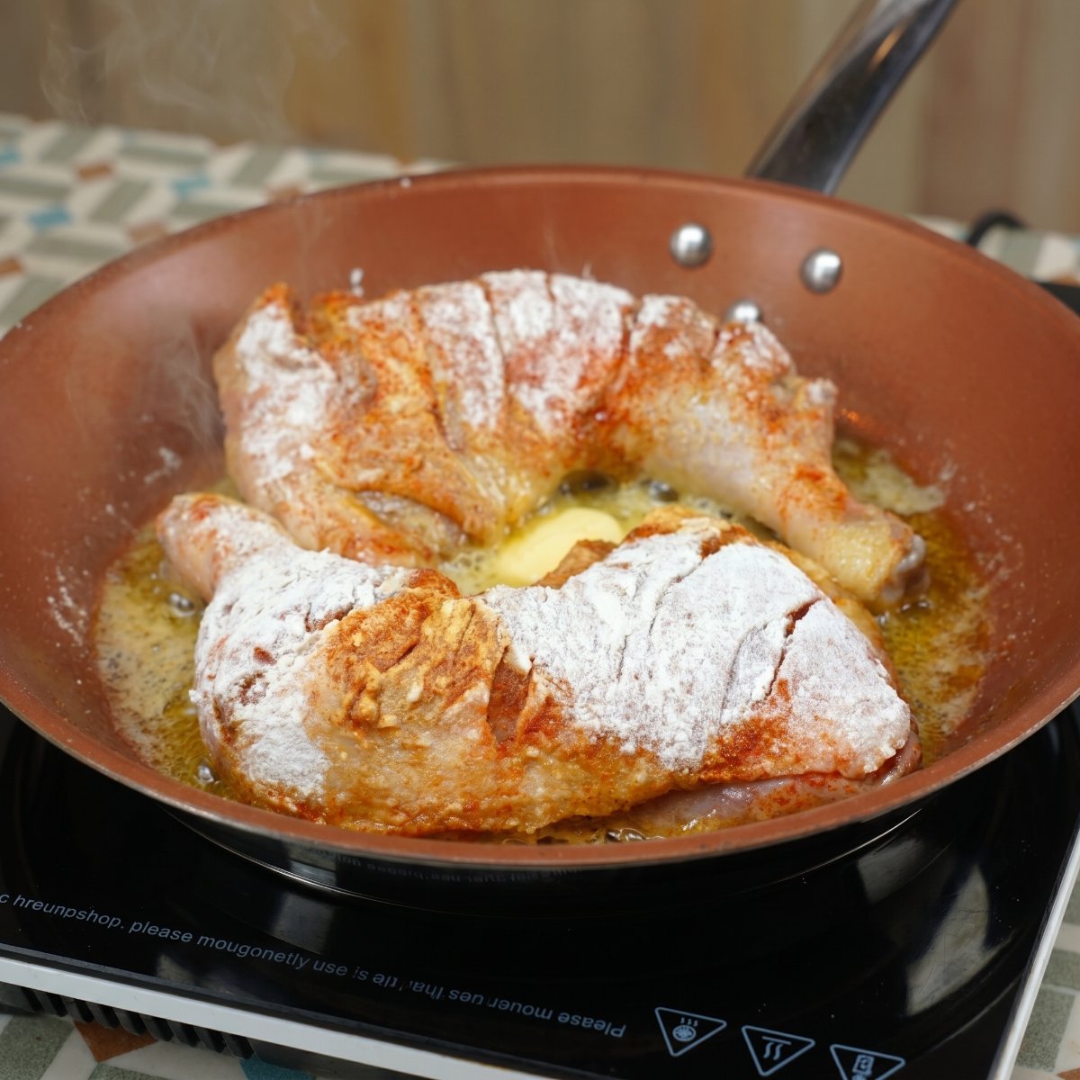 Zwei mehlierte und gewürzte Hähnchenkeulen braten in einer Pfanne mit geschmolzener, schäumender Butter.
