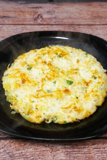 Omelette au poulet et pommes de terre, avec des oeufs et des pommes de terre râpées, parsemée d'herbes fraîches, servie dans une assiette.