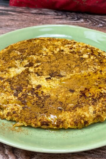Bananen-Haferflocken-Pfannkuchen mit Zimt bestreut und mit etwas Honig beträufelt, auf einem Teller serviert.