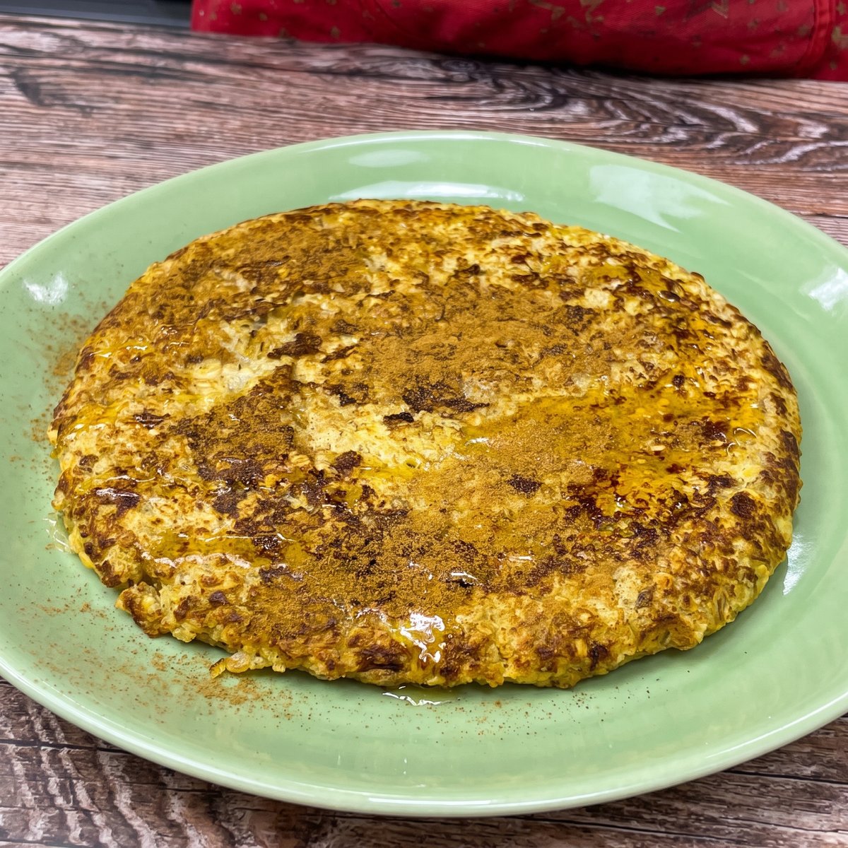 Bananen-Haferflocken-Pfannkuchen mit Zimt bestreut und mit etwas Honig beträufelt, auf einem Teller serviert.