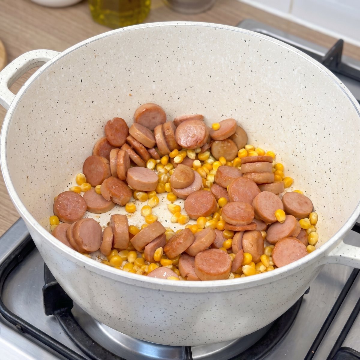 Popcornmais und Würstchenscheiben werden in einem Topf für Popcorn mit Würstchen zubereitet.
