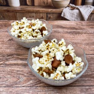 Two glass bowls filled with popcorn and pieces of fried sausage being served.