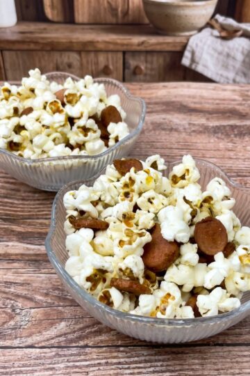 Two glass bowls filled with popcorn and pieces of fried sausage being served.