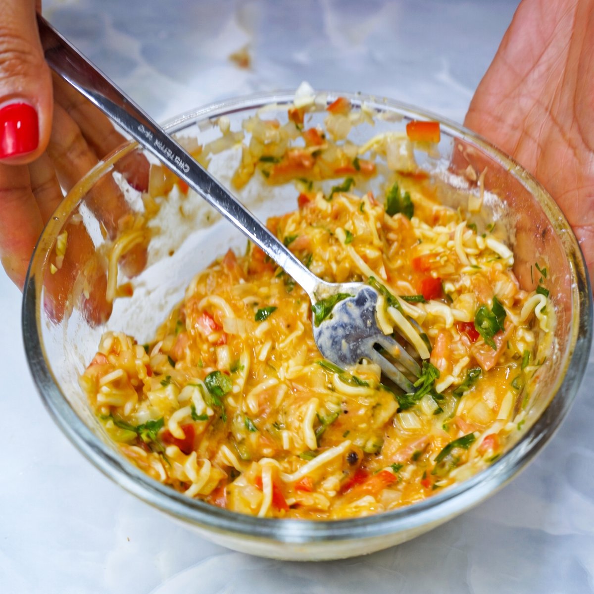 Hands holding a glass bowl with tuna and mozzarella omelet ingredients being mixed with a fork.