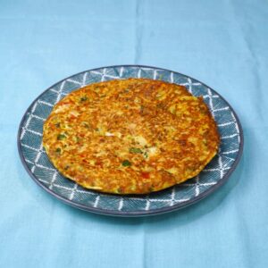 Plated tuna and mozzarella omelet, golden and served with pieces of vegetables.