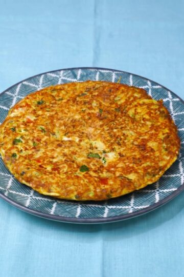 Plated tuna and mozzarella omelet, golden and served with pieces of vegetables.